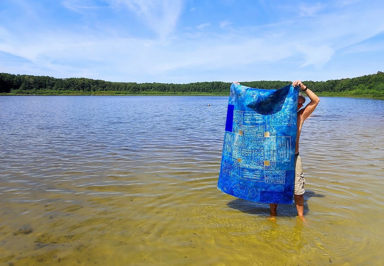 A person holding a blue painted canvas while standing in shallow water
