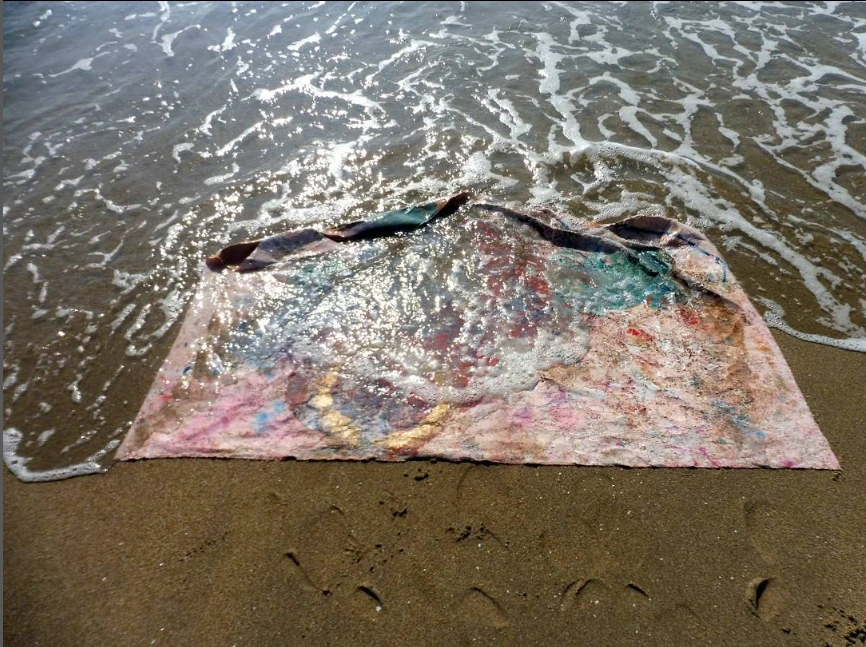 A painted work laid at the water’s edge as a wave reaches its surface