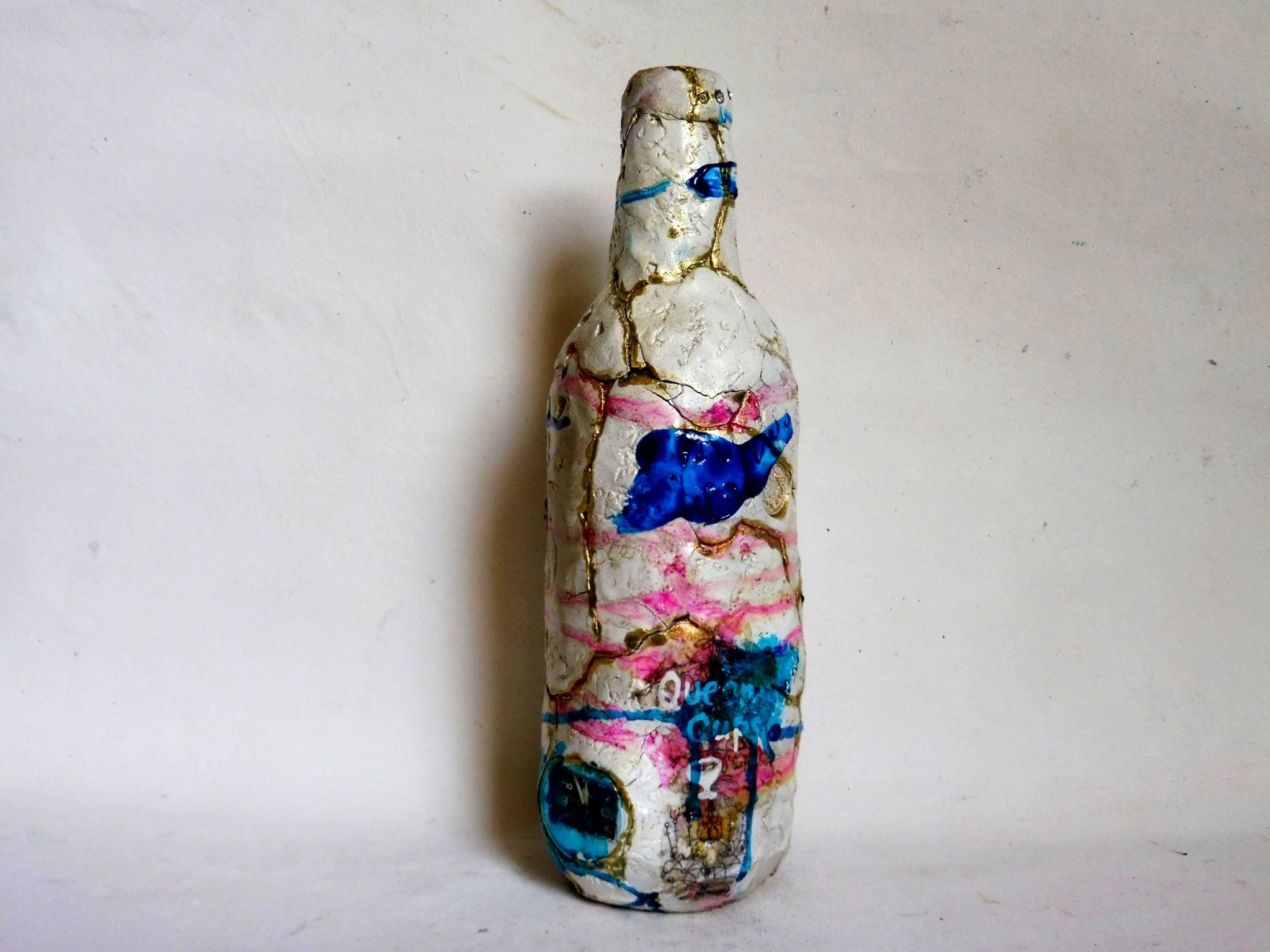 Close view of a clay-covered bottle with blue areas, red lines and embedded materials