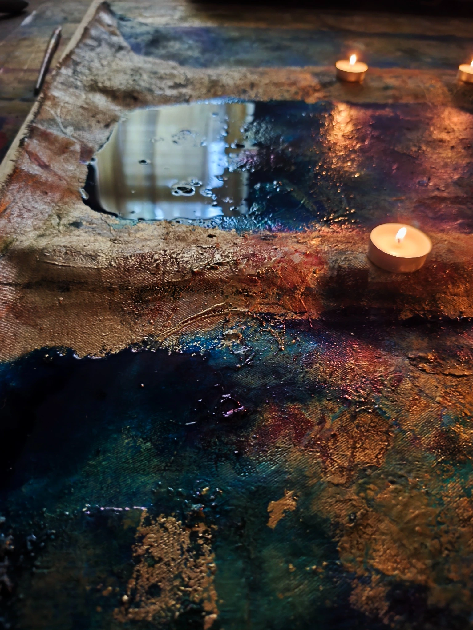A reflective rectangular object and lit candles arranged on a painted surface