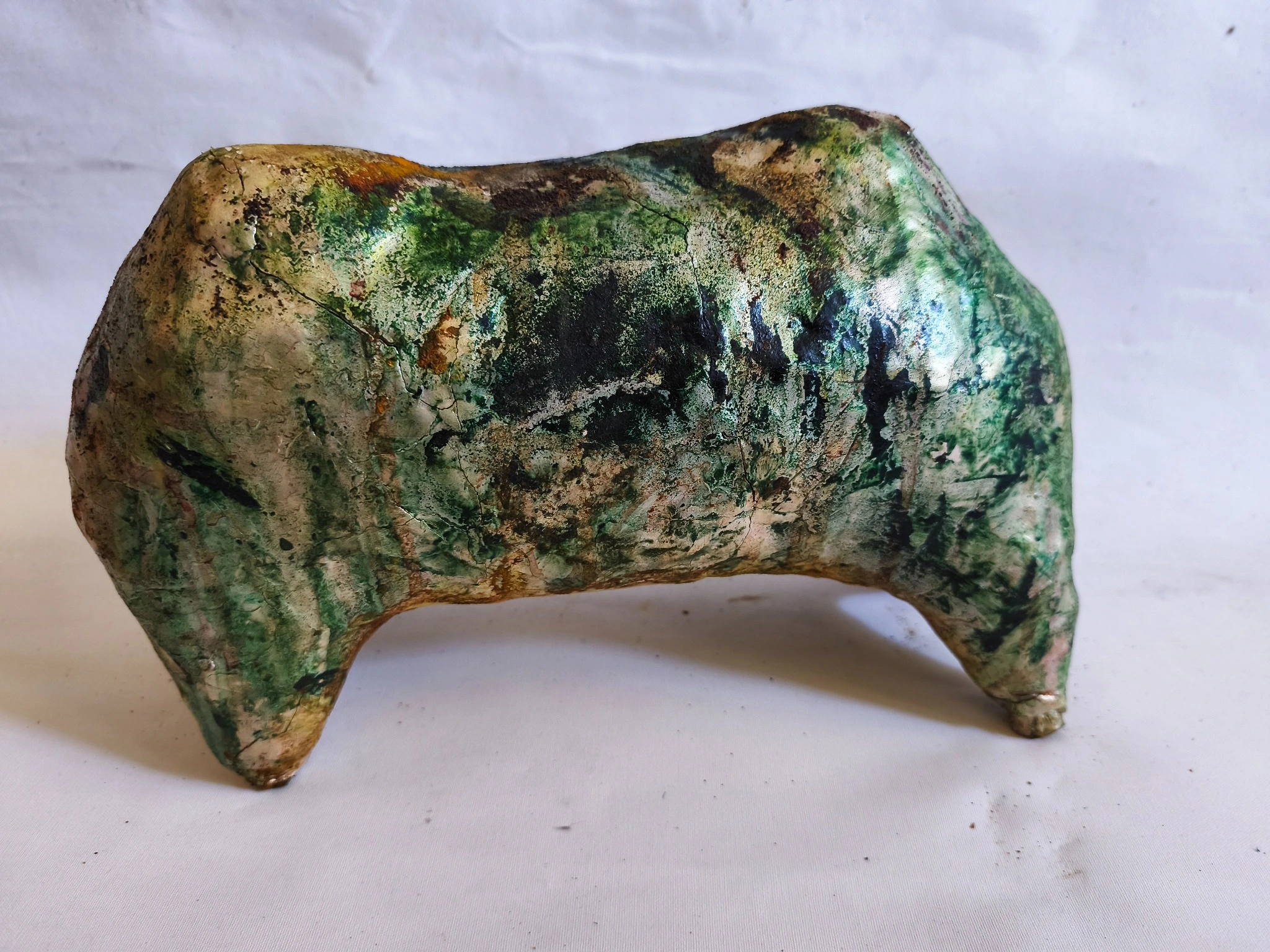 Arched clay object with mottled green, brown and pale surfaces