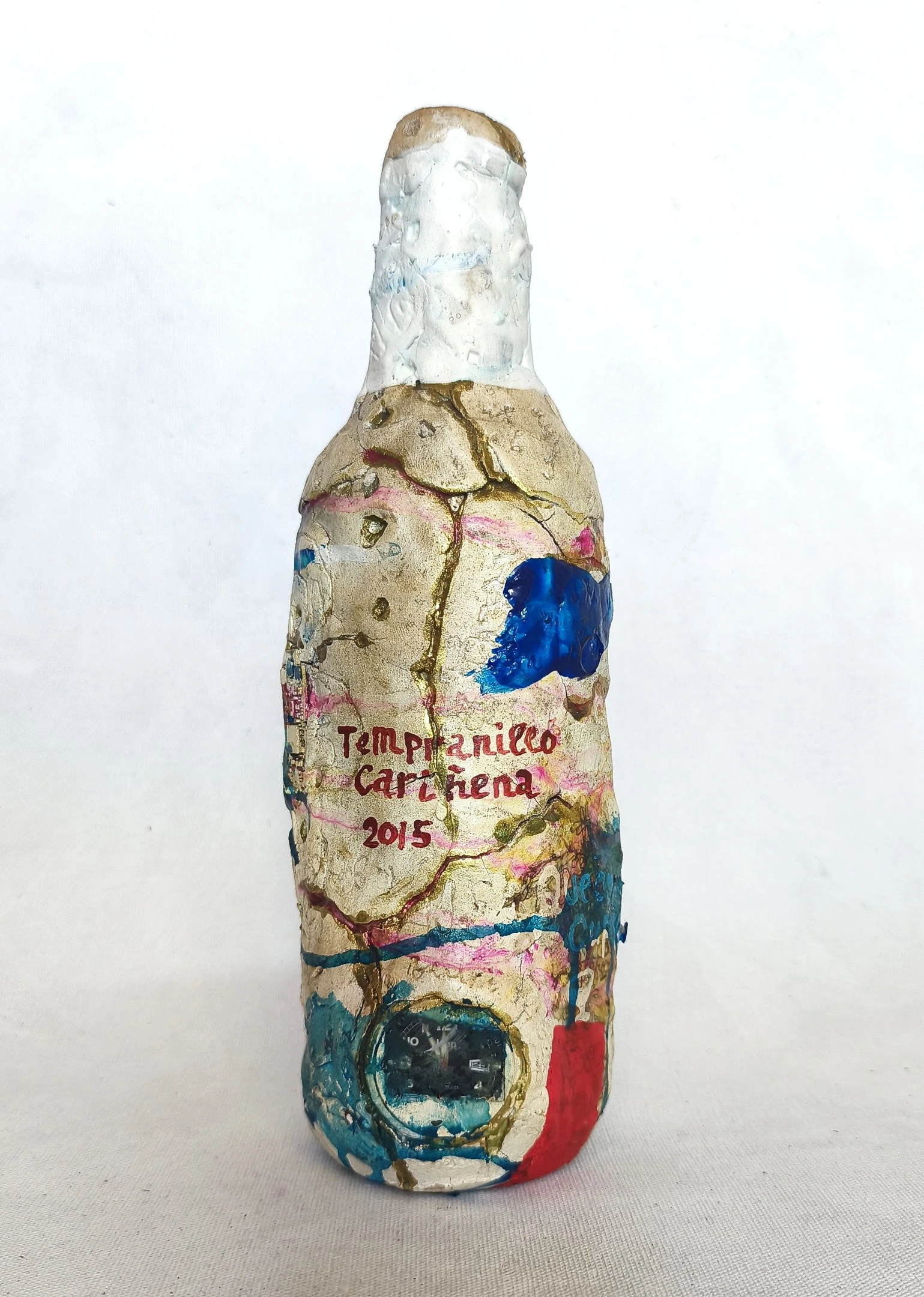 A wine bottle transformed by clay, pigments, marks and embedded materials